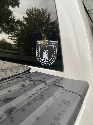 Close-up of the white Men in the Arena shield decal applied to a truck's back window